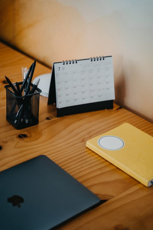 A laptop and paper calendar on a wooden desk, representing a content planning workflow