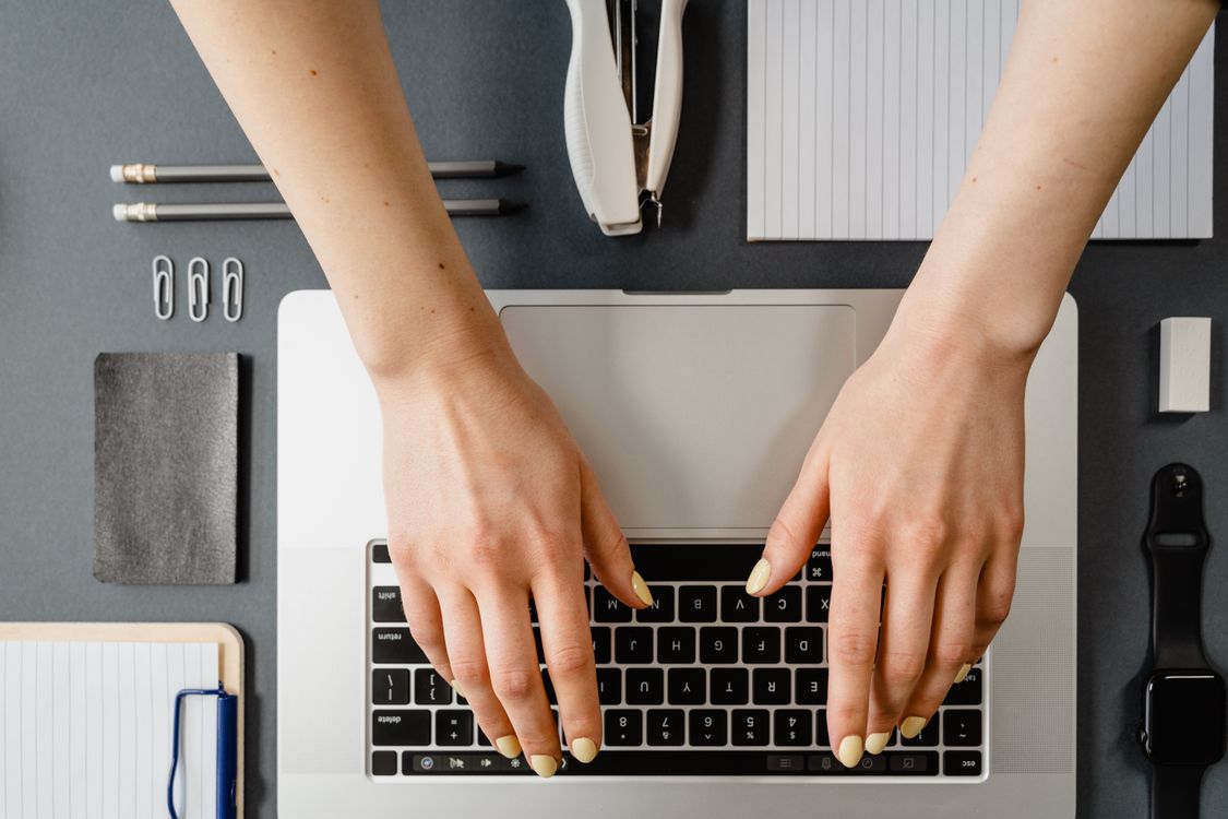 Person typing on a laptop at a minimalist desk with stationery nearby