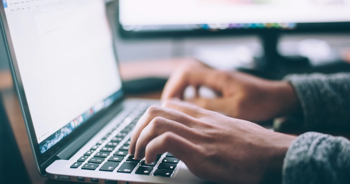 Hands typing on a laptop keyboard while drafting content