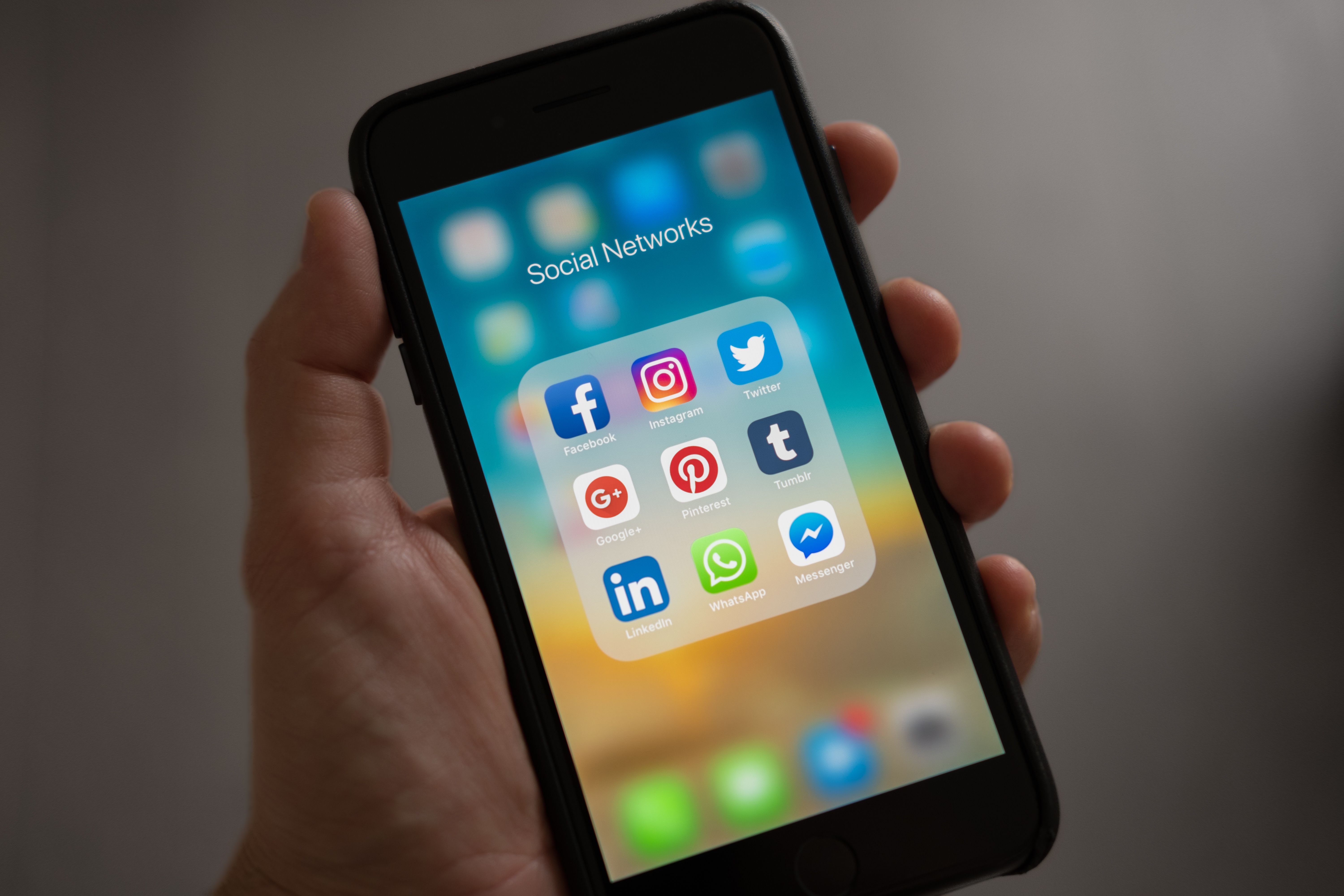 Person holding a smartphone showing social media app icons including Facebook and Instagram