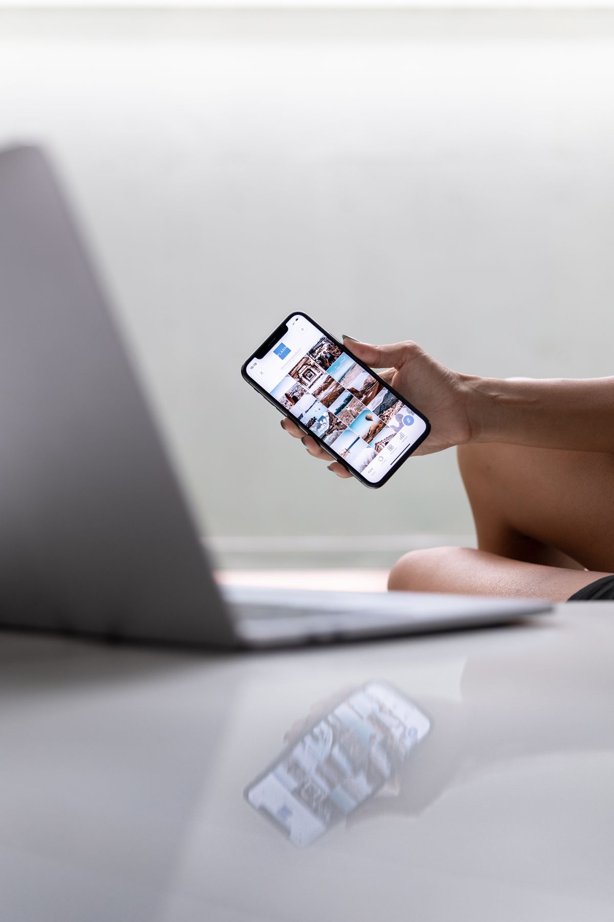 A person managing social media on a smartphone and laptop in a modern workspace