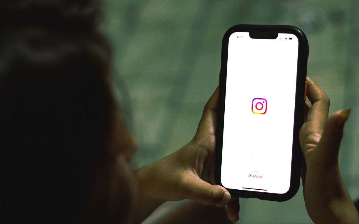 Close-up of a hand holding a phone showing the Instagram app icon