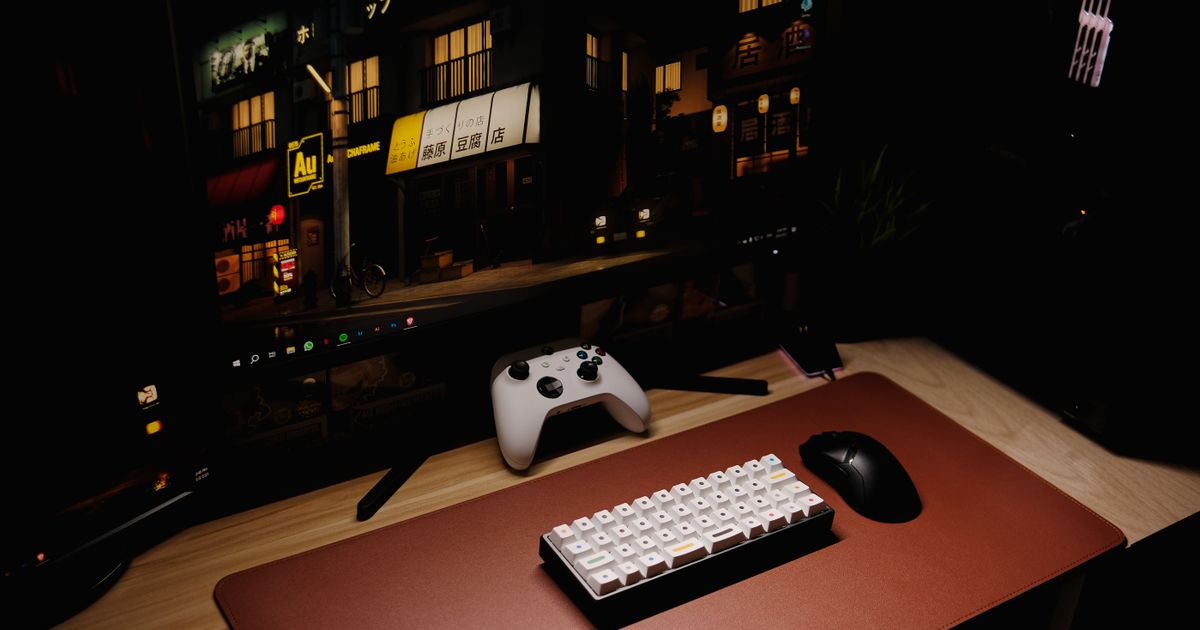 A gaming keyboard, mouse, and controller arranged on a desk near a monitor