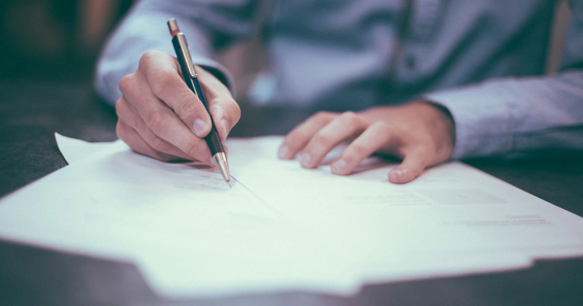 شخص يعبئ أوراقاً رسمية على مكتب مع مستندات وقلم