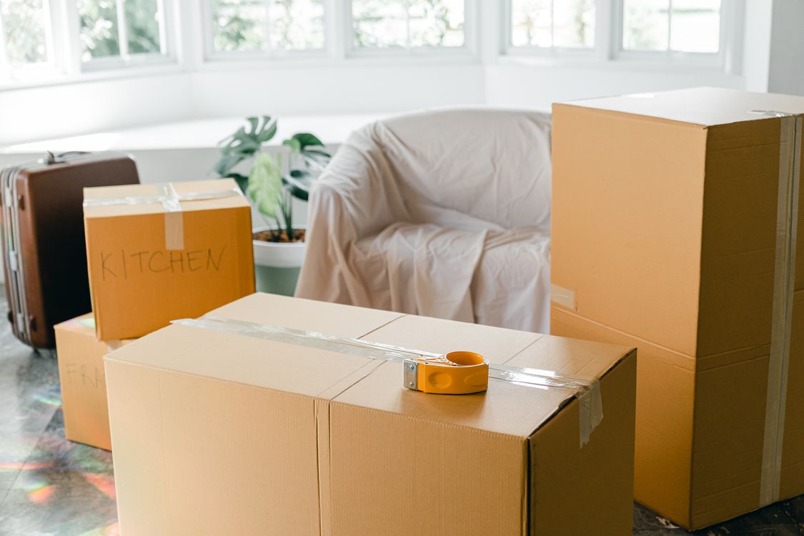Labeled cardboard moving boxes stacked in a sunlit empty apartment ready for relocation.