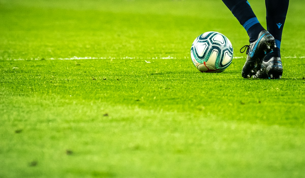 A football on the green grass of a stadium pitch with seating visible in the background