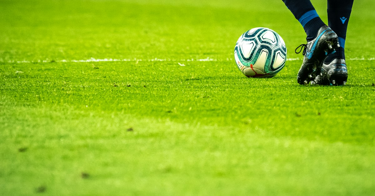 Football on a grass pitch with stadium seating in the background