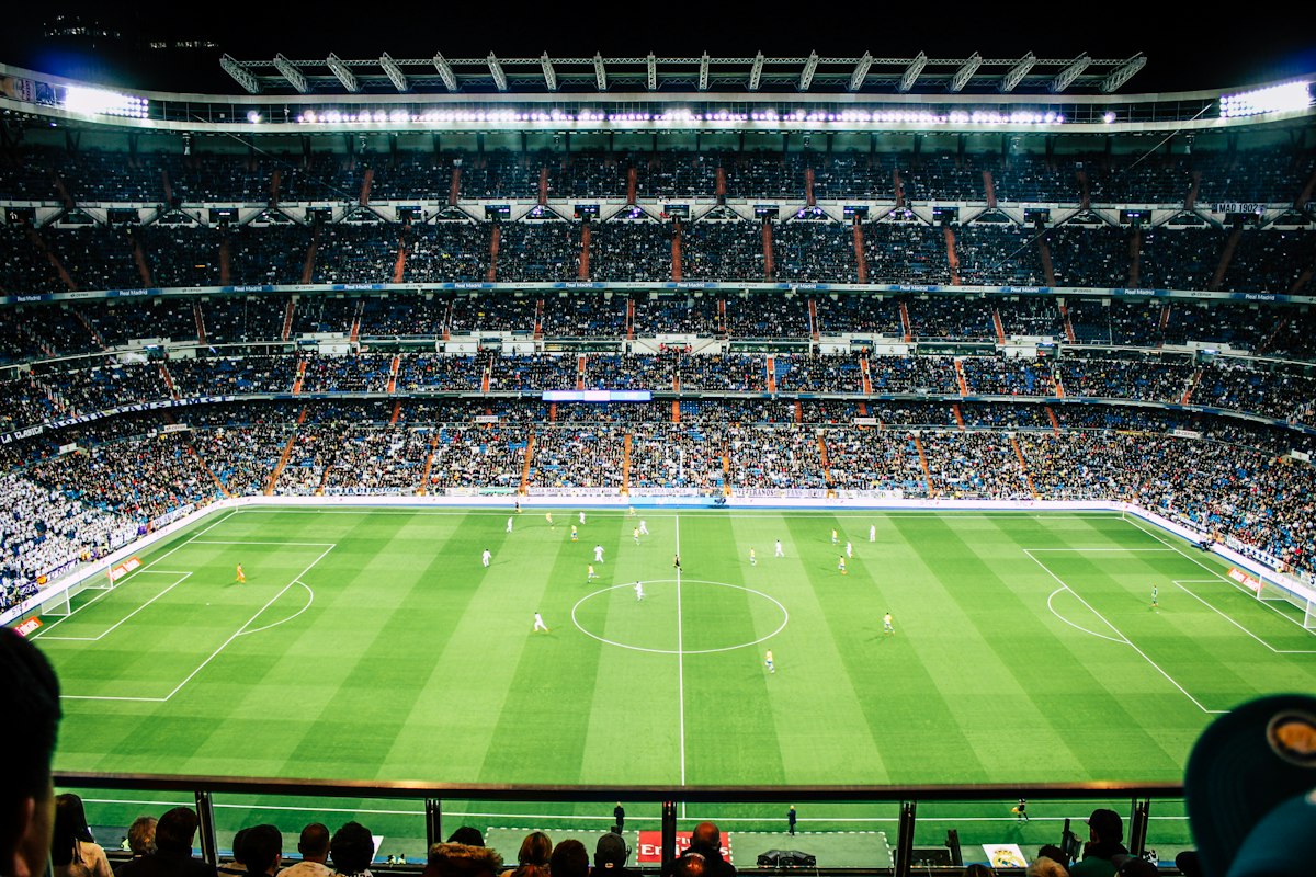 Packed football stadium at night during a professional match with floodlights illuminating the pitch