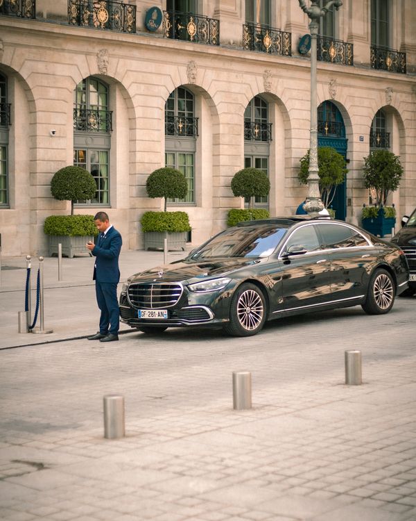 Professional chauffeur in a black suit standing beside a luxury black sedan on a city street
