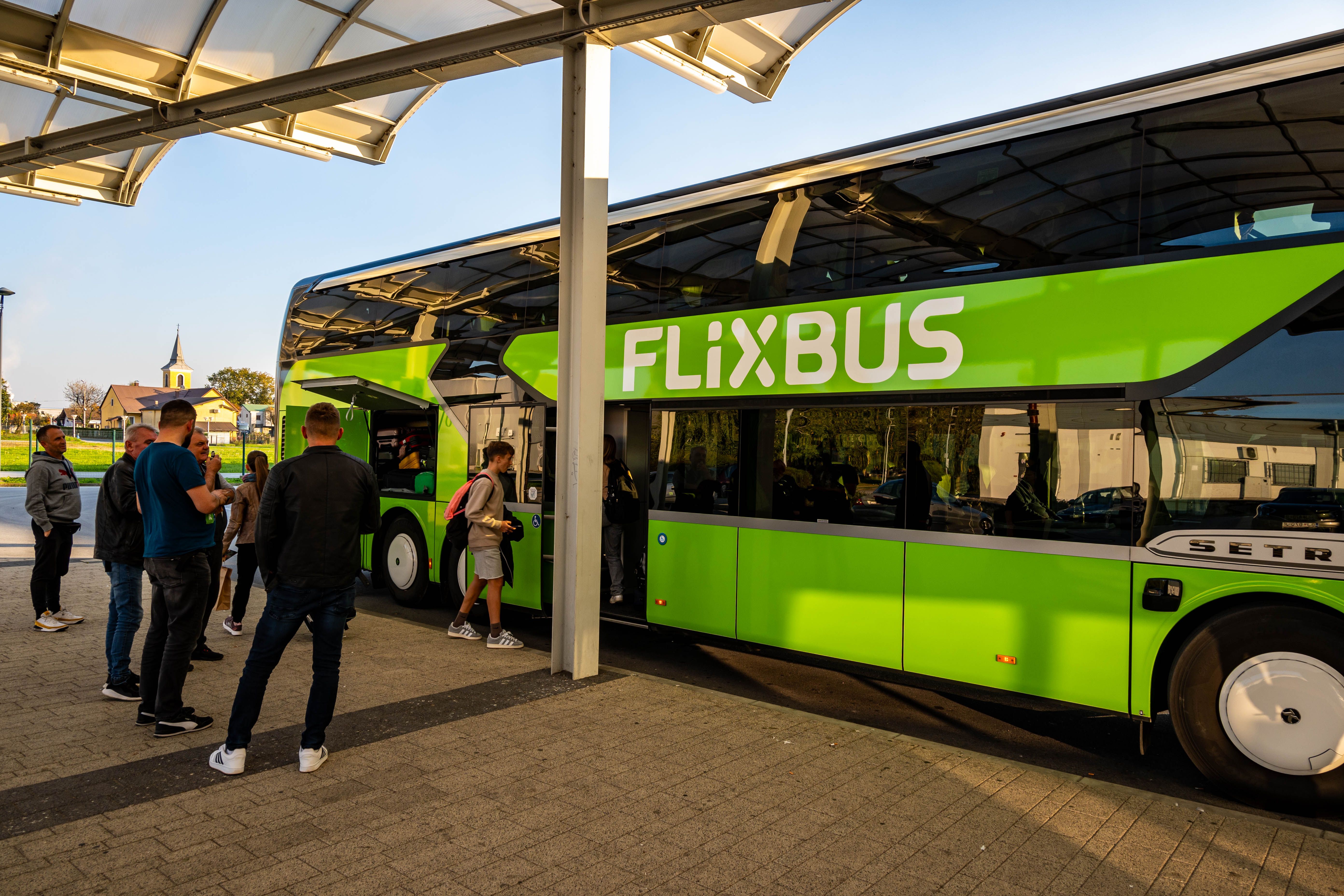 Passengers queue to board a shuttle coach at a covered station platform