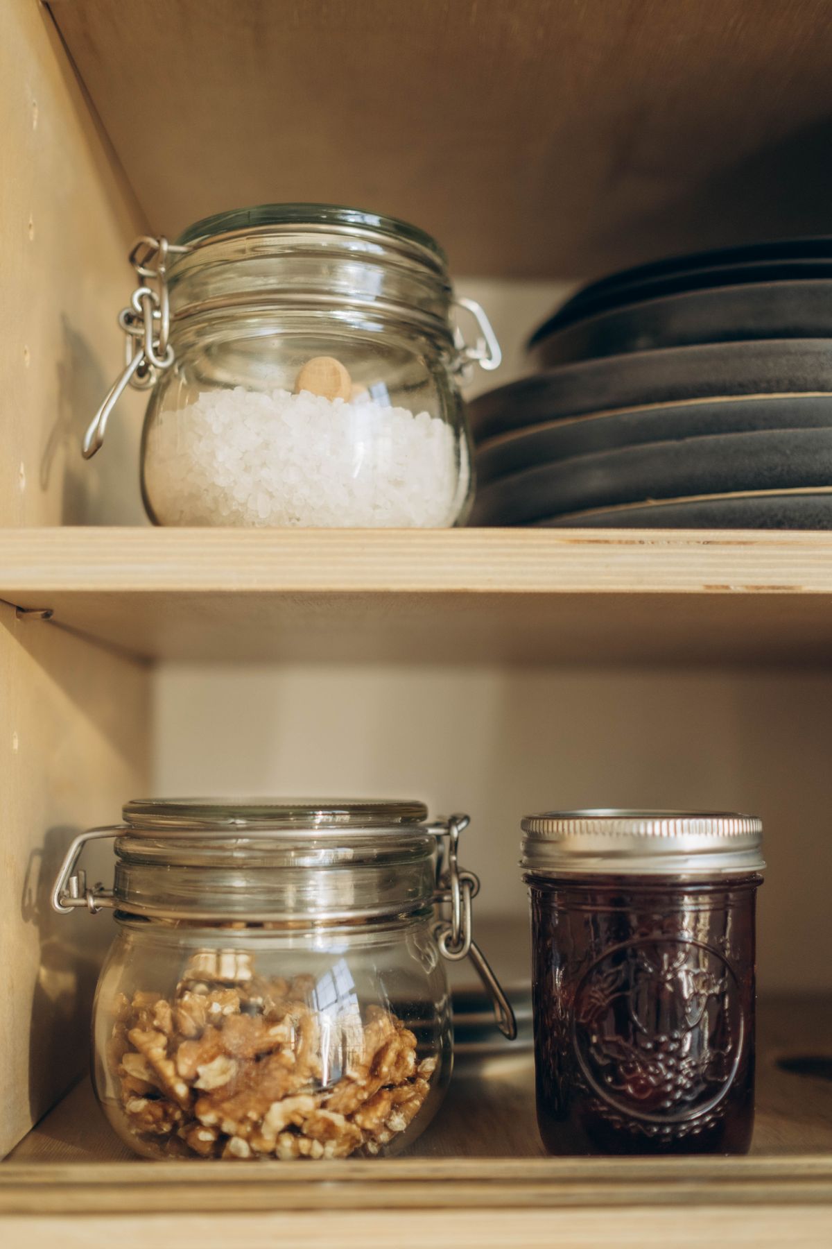 Glass storage jars neatly arranged on white pantry shelves holding dry goods and preserves