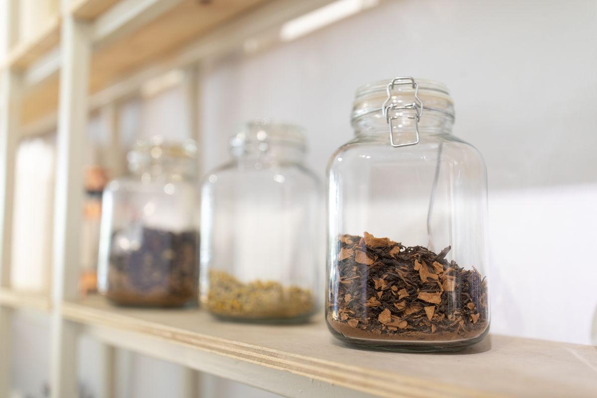 Clear glass jars filled with dried herbs and spices on a rustic wooden kitchen shelf
