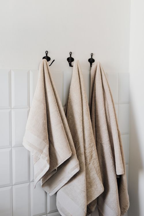 Beige towels hanging on wall hooks in a tiled bathroom