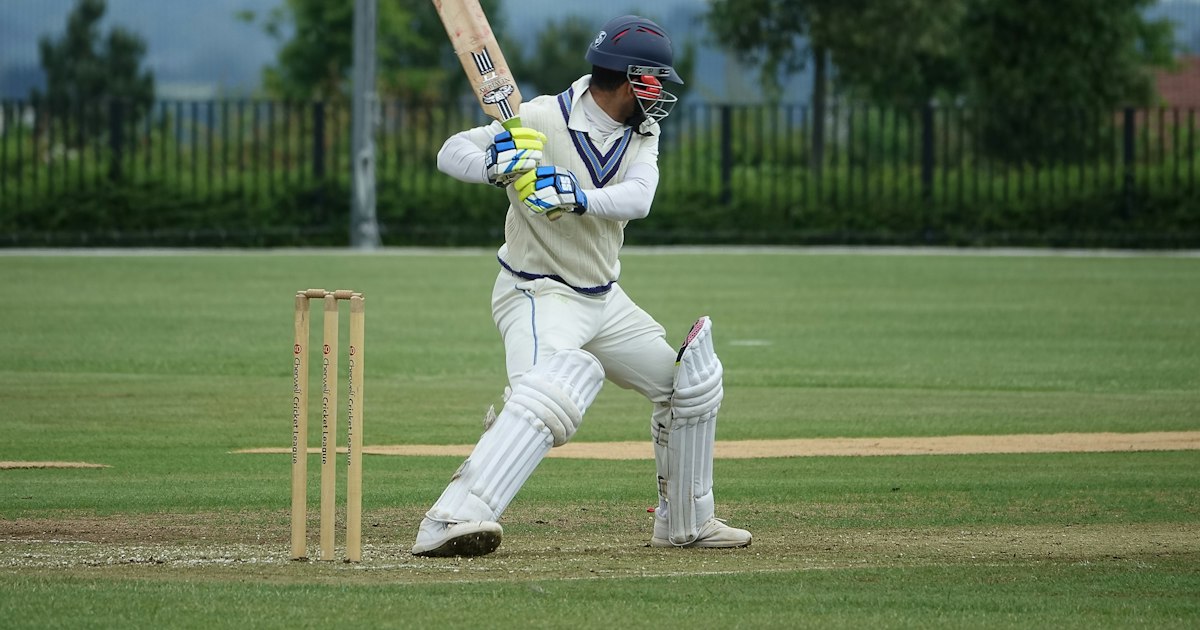 Cricket batsman preparing to face a delivery on a green pitch