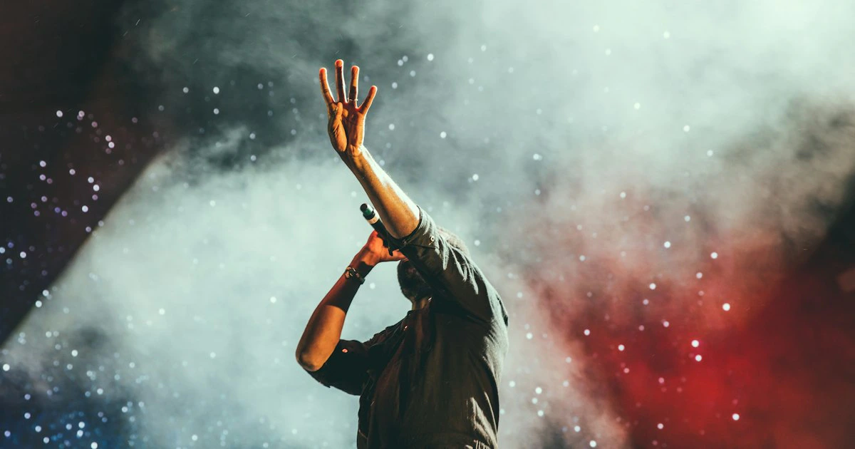 Performer silhouette on stage with dramatic backlighting and concert crowd in foreground