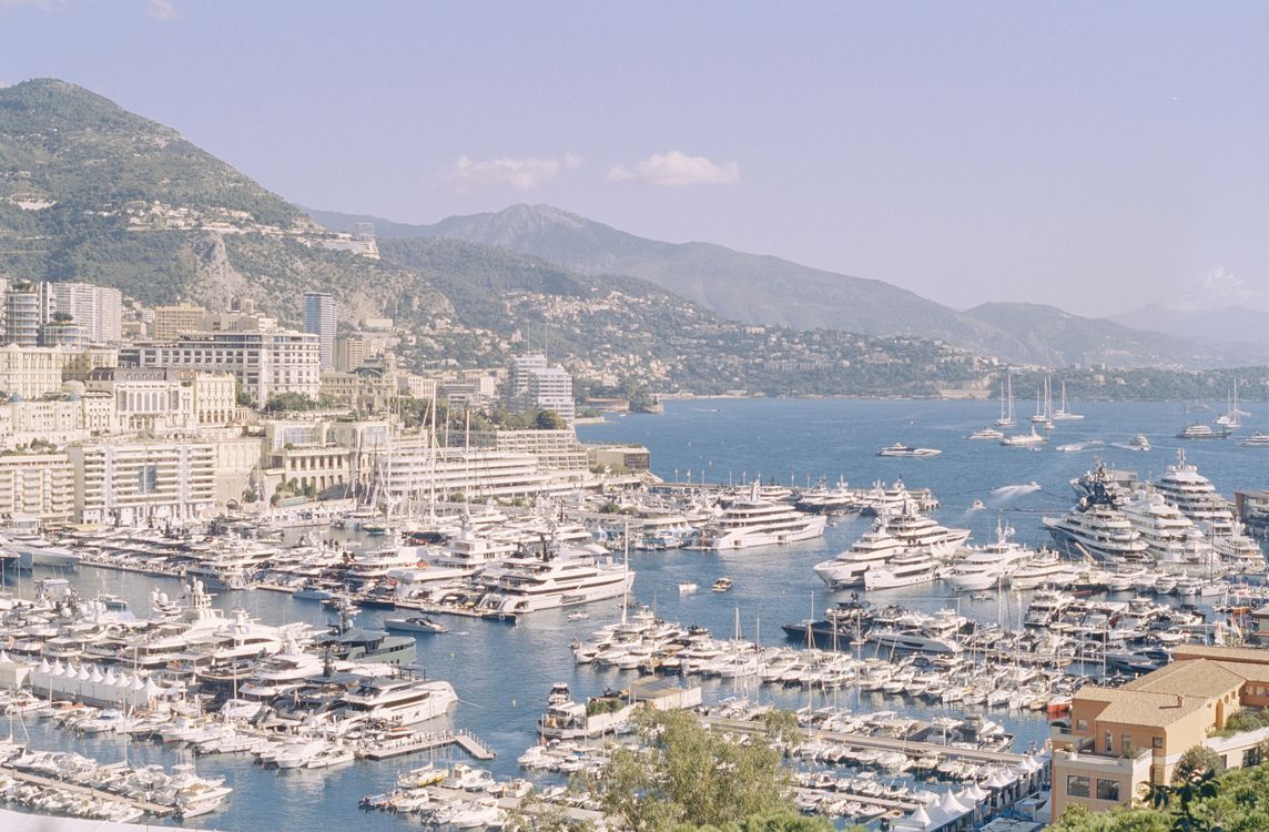 Aerial view of Monaco harbor filled with luxury yachts and scenic Mediterranean coastline.