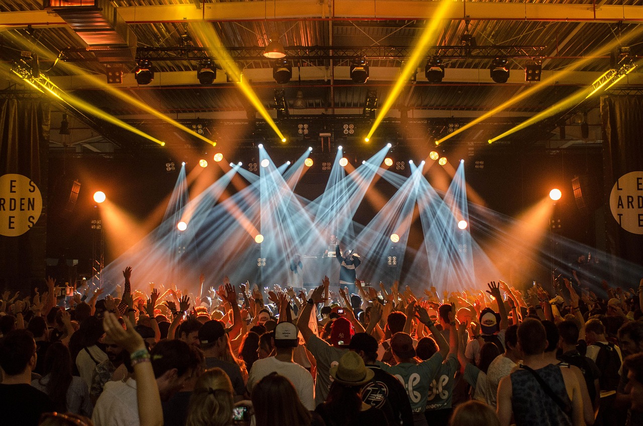 Concert crowd with hands raised under colorful stage lights