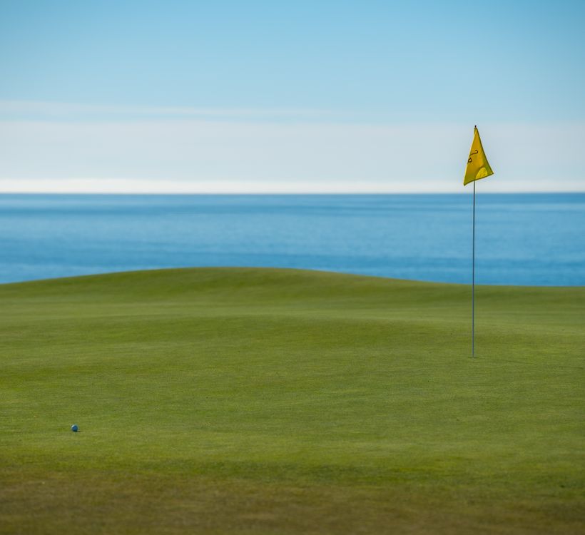 Scenic oceanside golf course with putting green and flag under blue skies