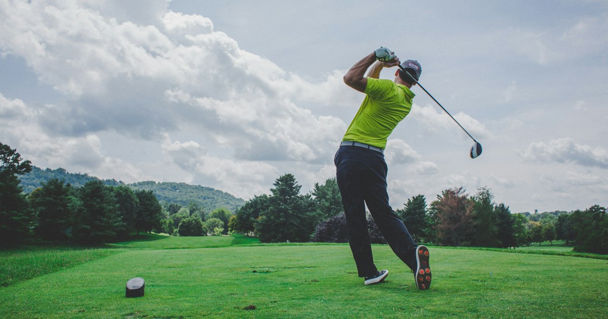 Lush green golf course fairway lined with mature trees under a blue sky.