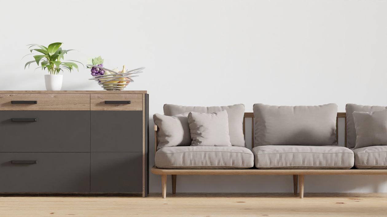 Beige sofa with throw pillows beside a wooden chest of drawers in a minimalist interior