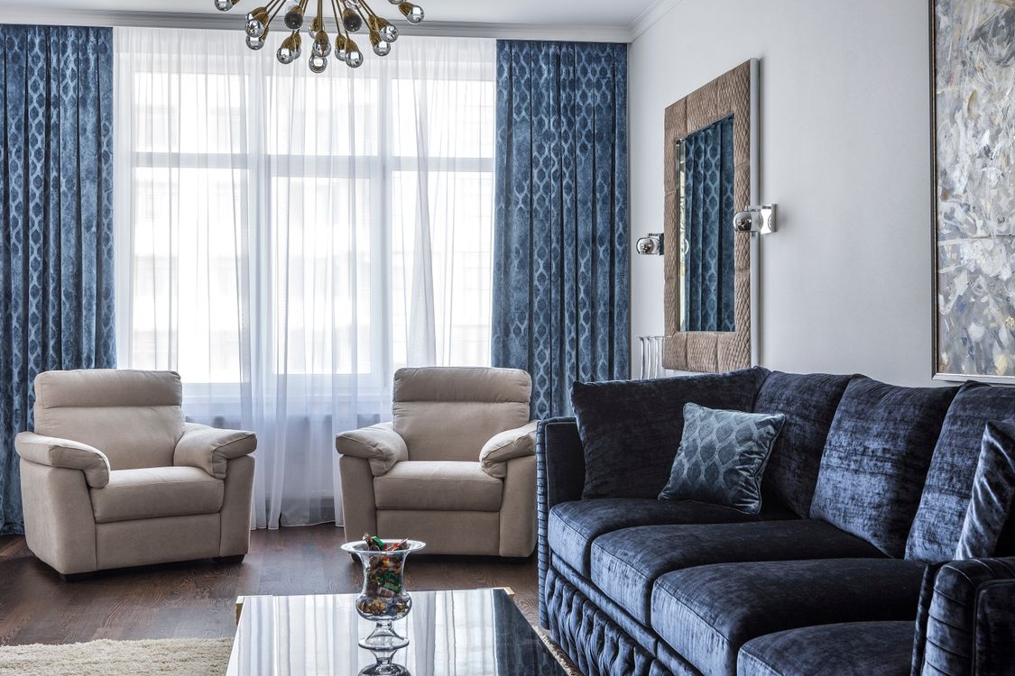 Elegant modern living room with a blue sofa, beige armchairs and a contemporary chandelier