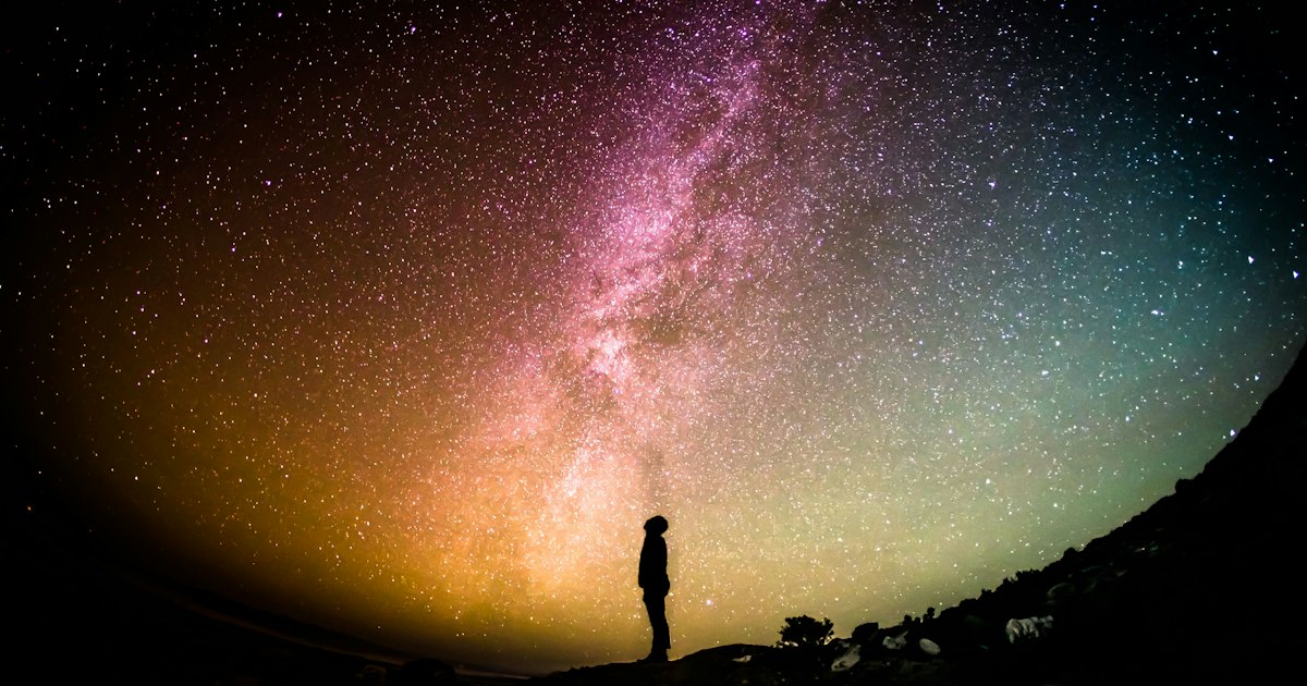 Persona de pie frente a una vía láctea luminosa, contemplando el sentido de la vida