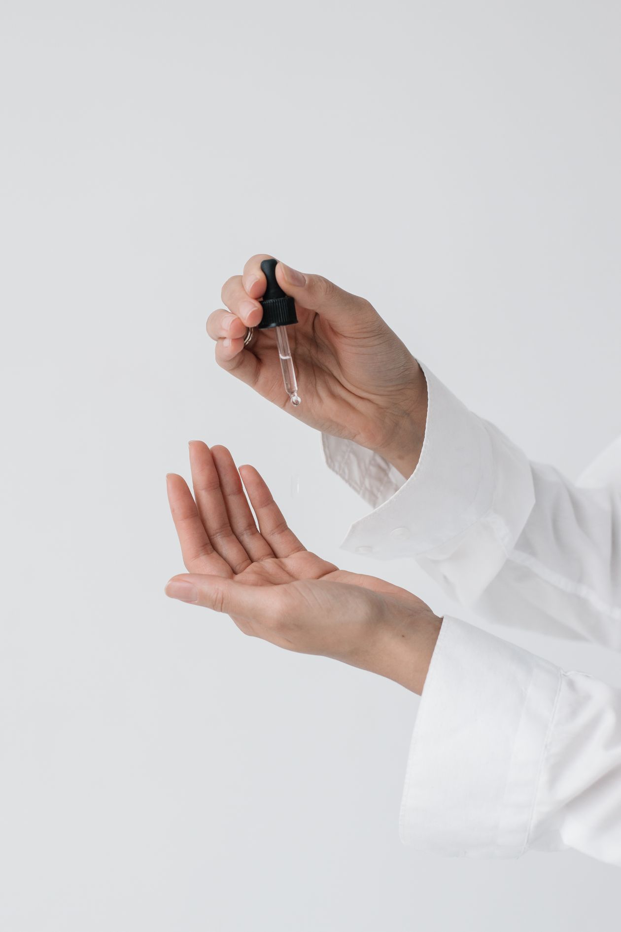 Hands applying skincare serum with a glass dropper