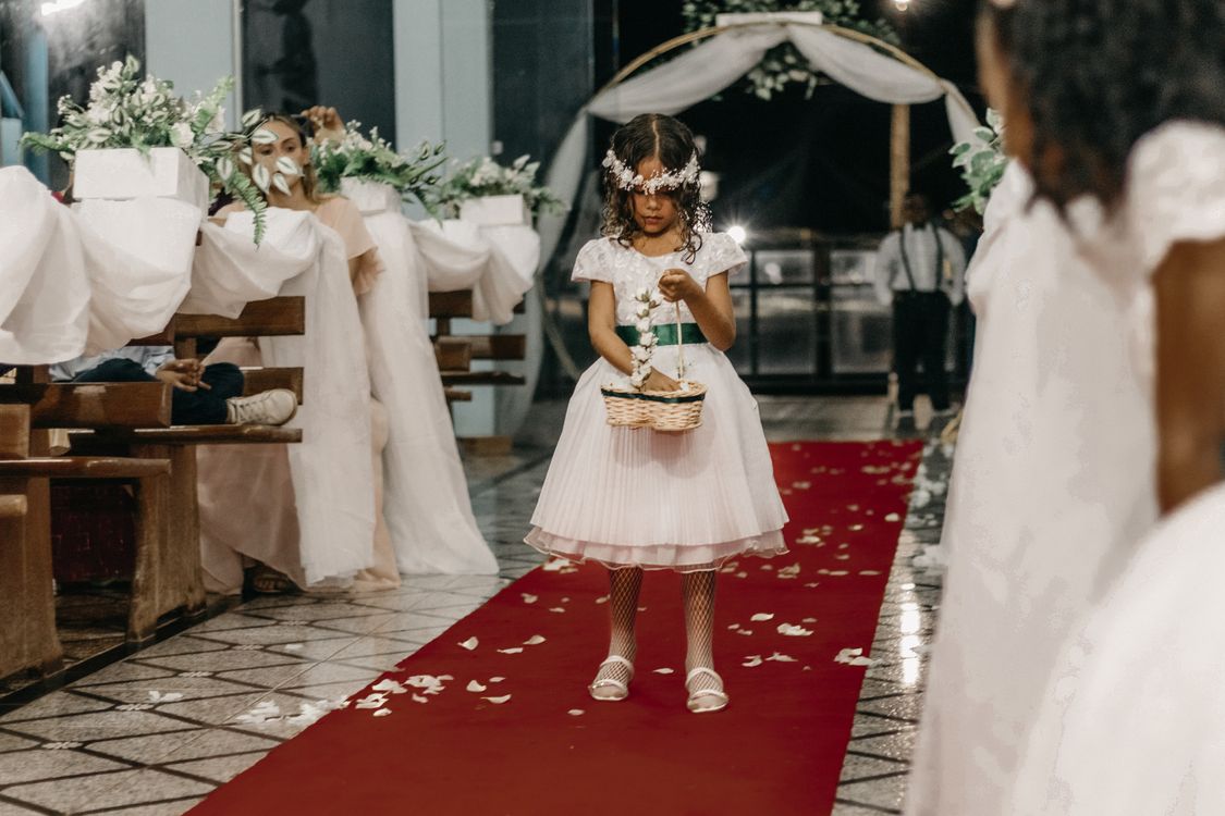 A young flower girl in a white dress scattering petals at a wedding ceremony