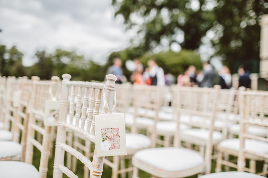 White wooden chairs arranged for an intimate outdoor wedding ceremony with greenery