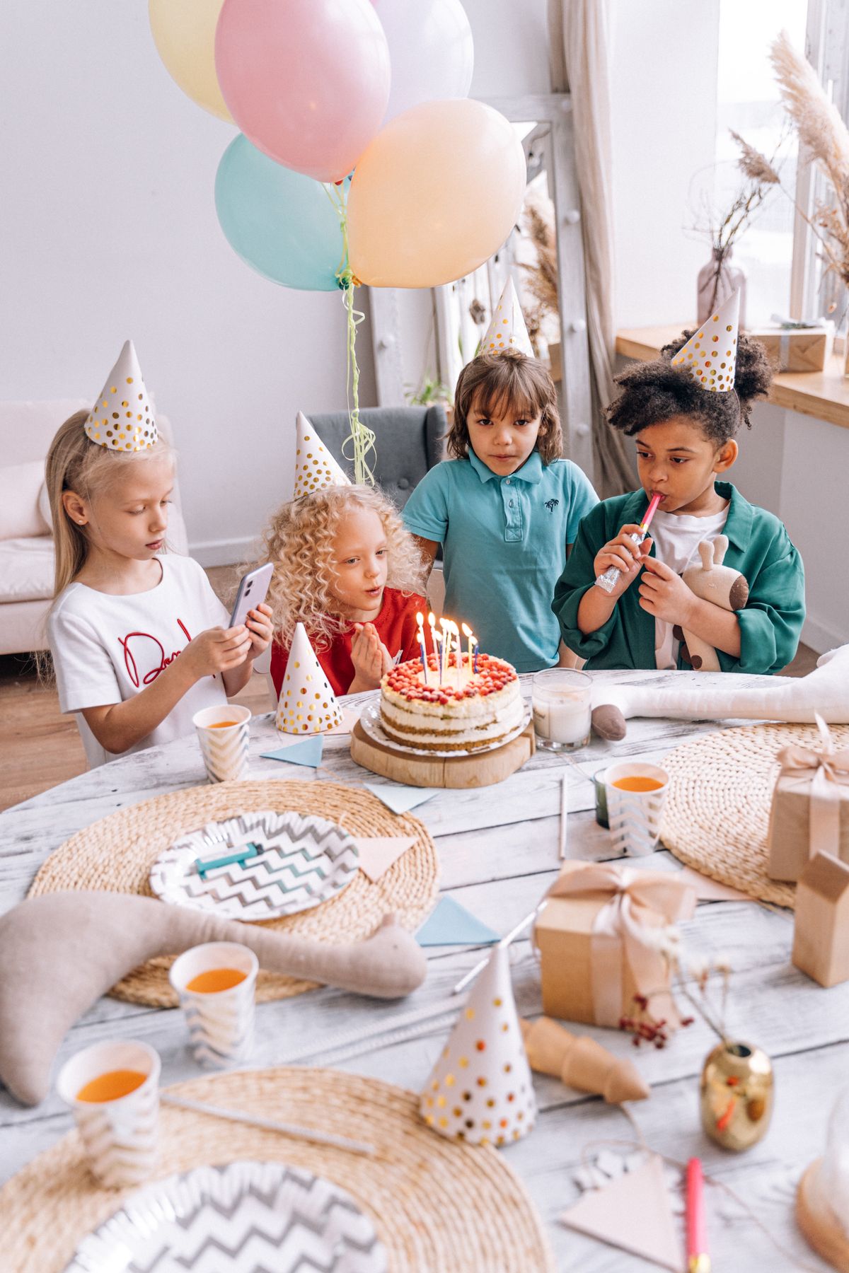 Children admiring a birthday cake with candles at a party with balloons and decorations
