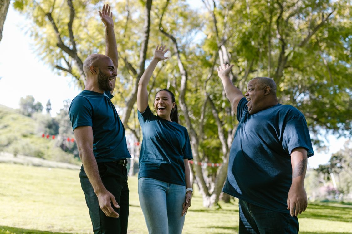 Diverse employees celebrating with arms raised during an outdoor team activity