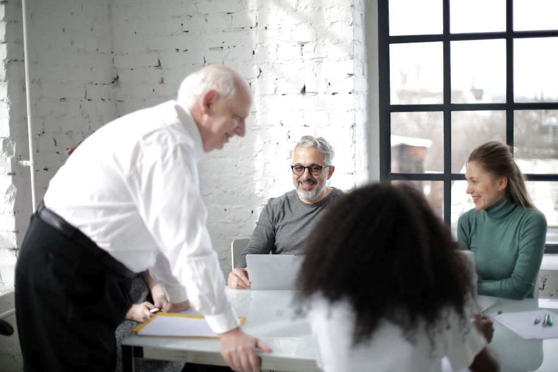 Business professionals collaborate around a table with laptops, reviewing operations work and approvals together.