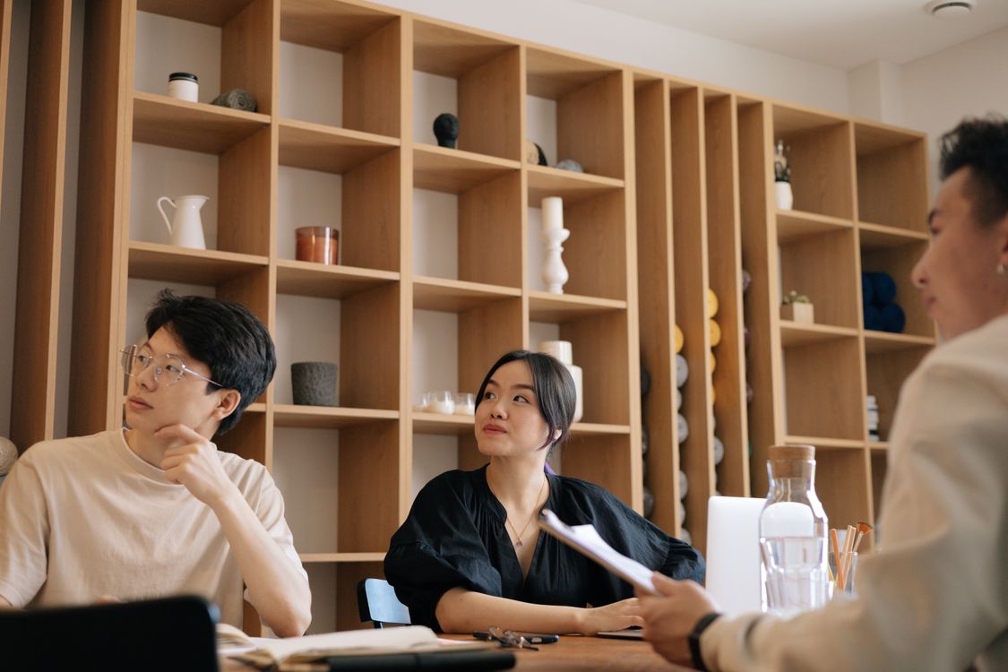 An office team gathers for a meeting in a bright modern workspace with digital devices visible, coordinating work across systems.