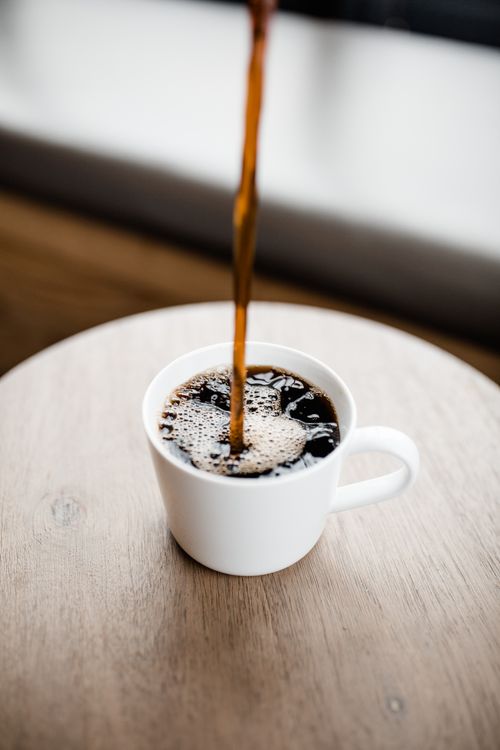 Steaming coffee poured into a white ceramic mug on a wooden table