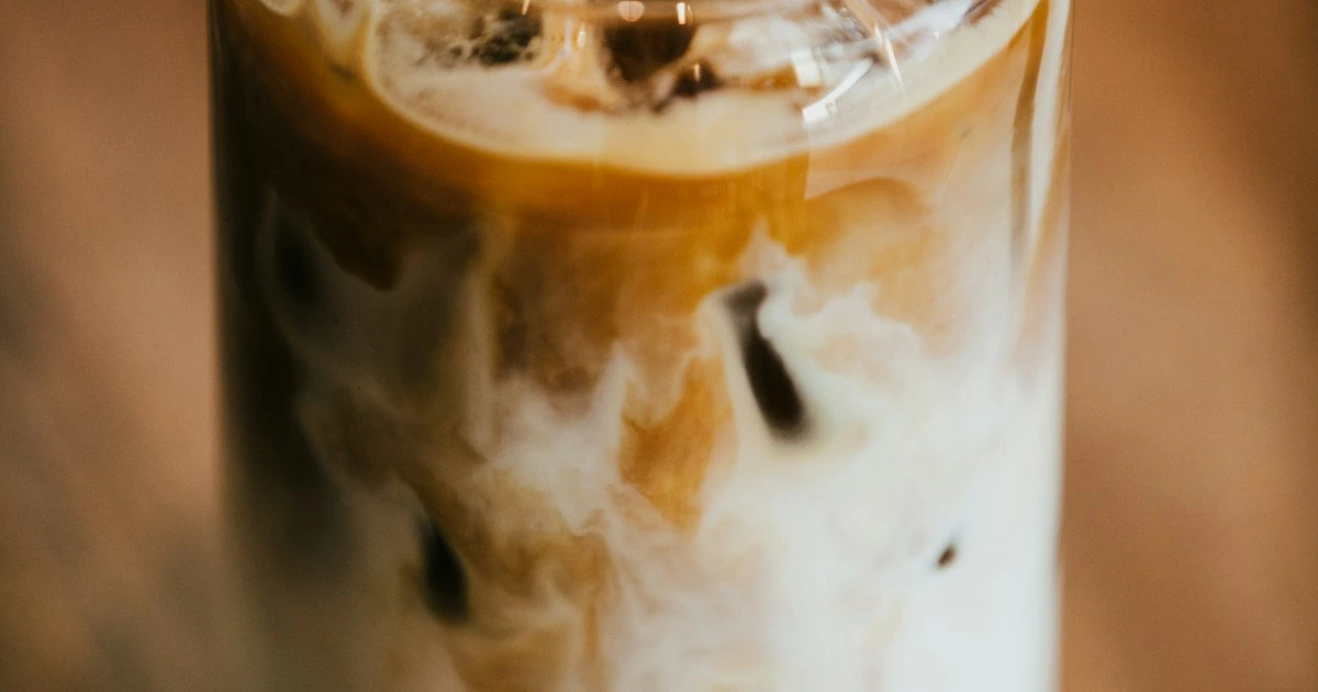 A tall glass of iced coffee with ice cubes and cream swirling through dark coffee