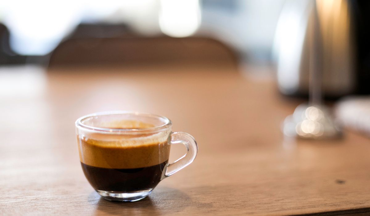 A freshly brewed cup of black coffee in a clear glass on a rustic wooden table