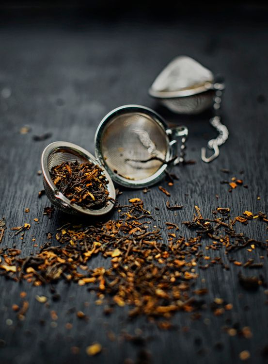 Loose dried tea leaves scattered beside a metal tea strainer