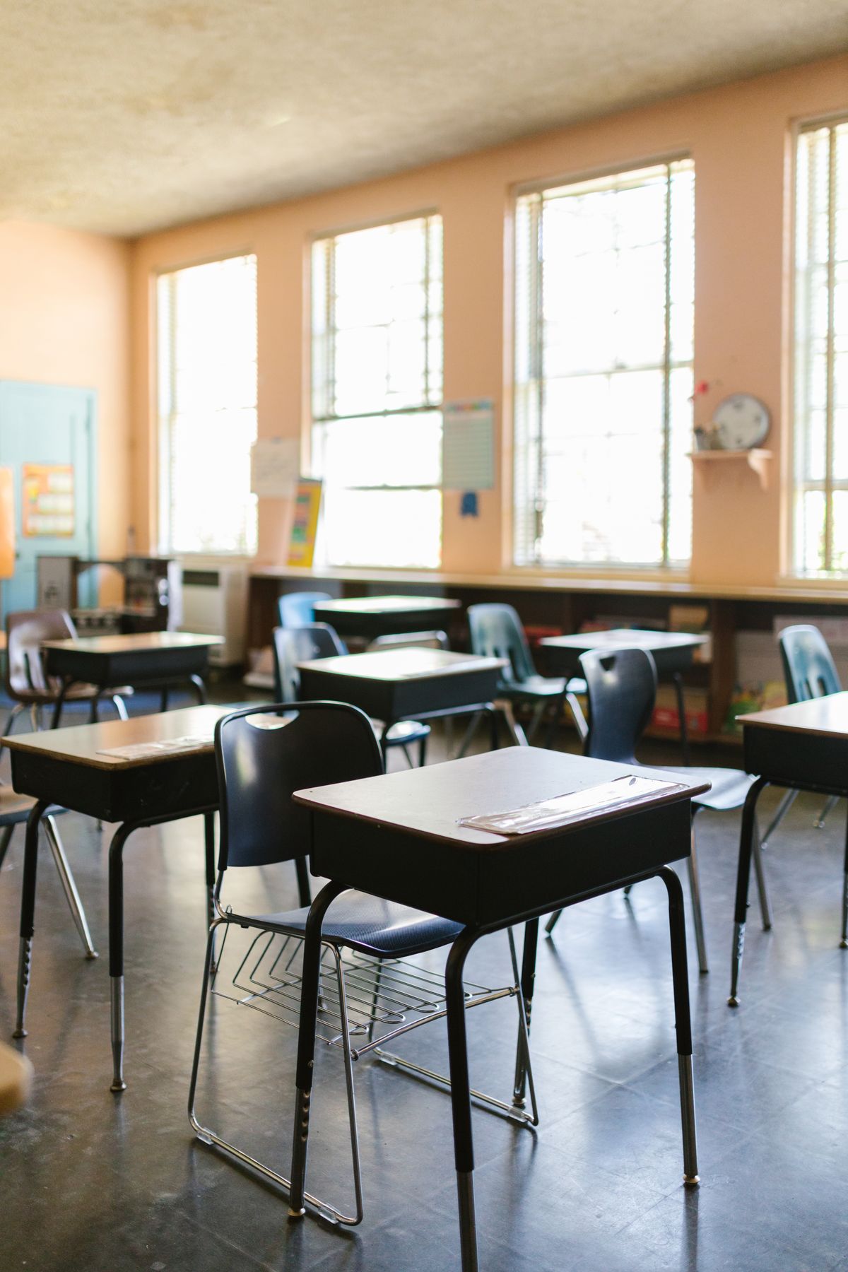 Rows of wooden school desks and chairs arranged in a sunlit classroom