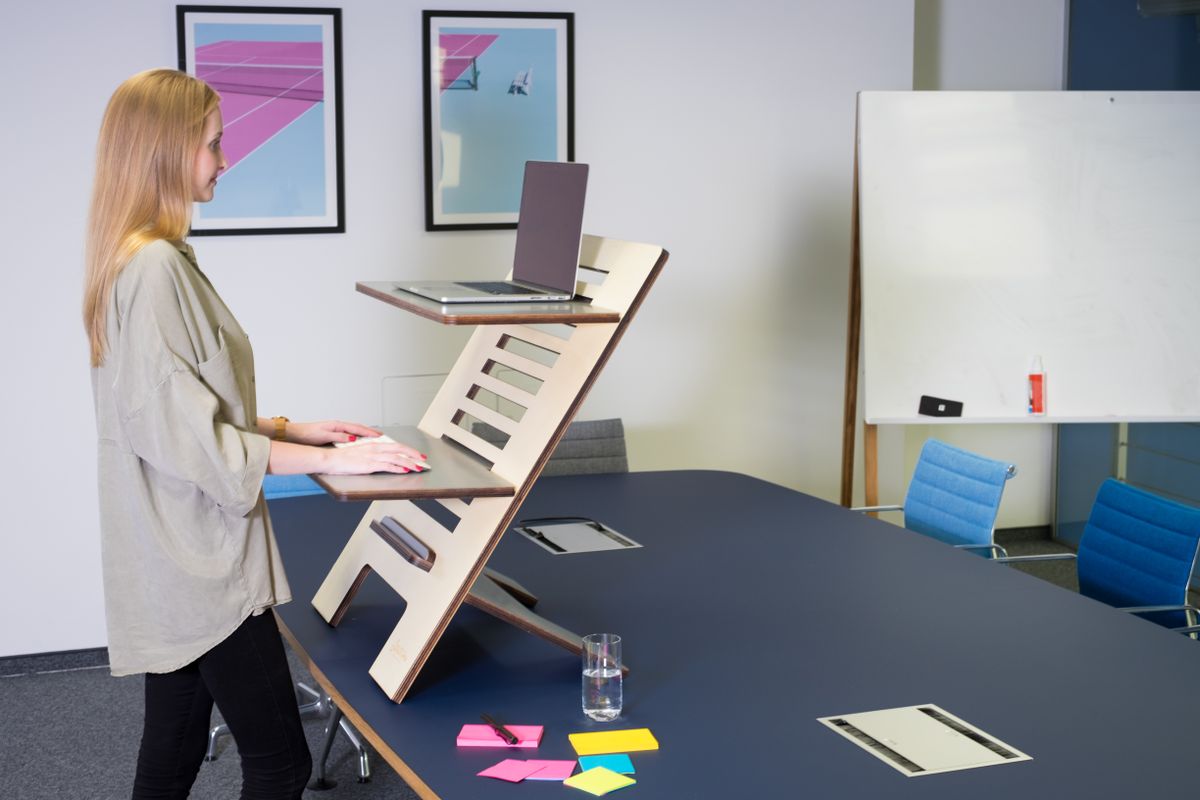 Professional woman working at a height-adjustable standing desk with a laptop in a modern office