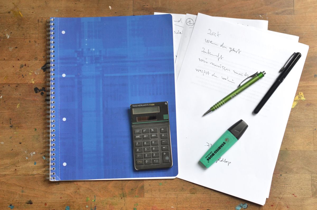Flat-lay of office supplies including a calculator, notebook and pens on a wooden desk