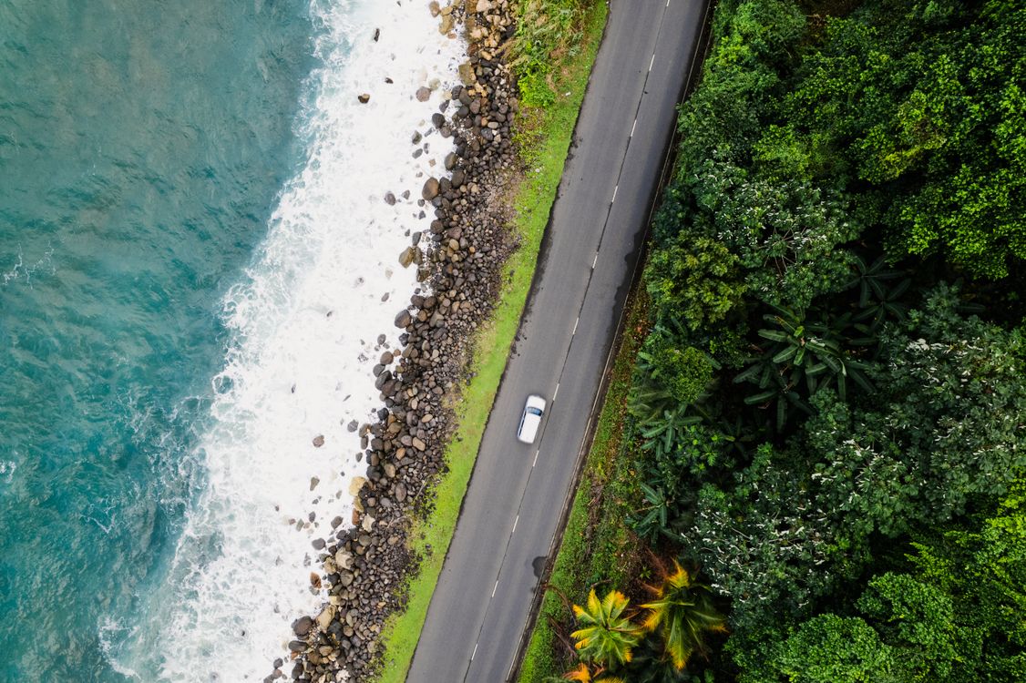 Aerial view of a car on a scenic coastal road in Costa Rica with ocean and greenery