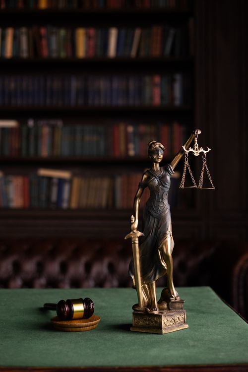 Estátua da Justiça com balança e martelo em biblioteca jurídica