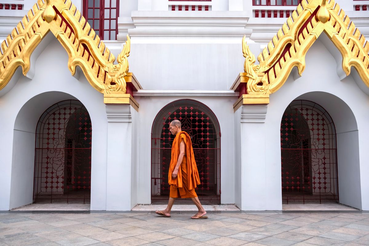 Buddhist monk in saffron robes walking past historic temple architecture in Bangkok