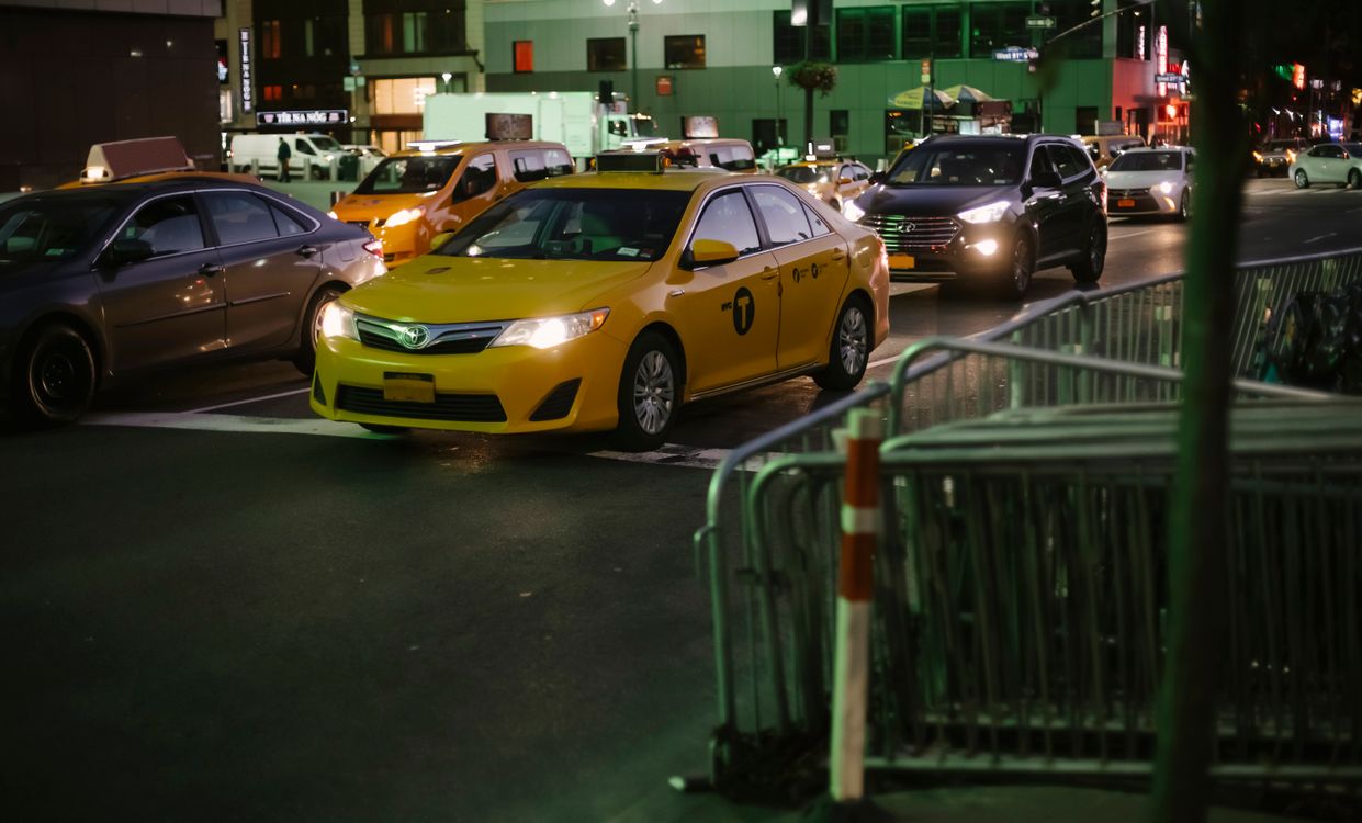 Taxi amarillo circulando entre el tráfico urbano al atardecer en una ciudad moderna.