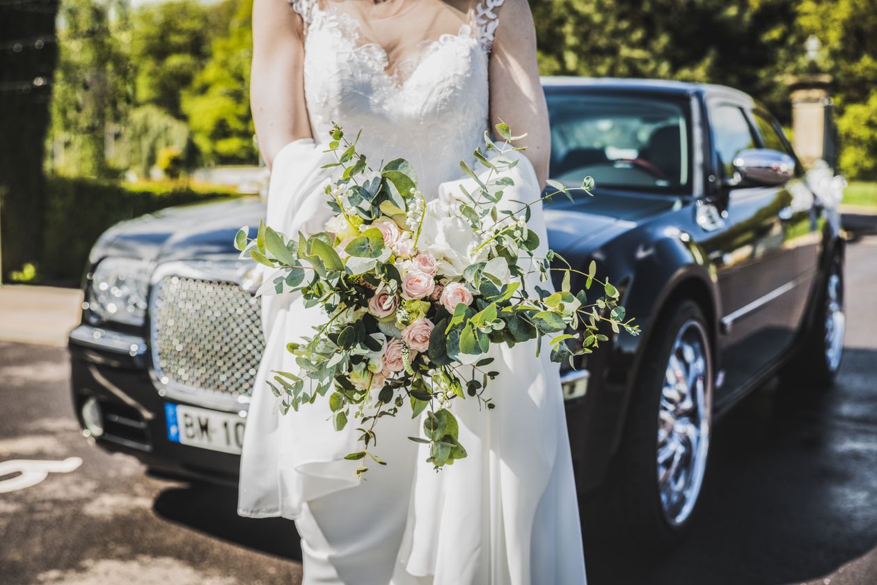 Novia con vestido blanco junto a un vehículo ejecutivo negro el día de su boda