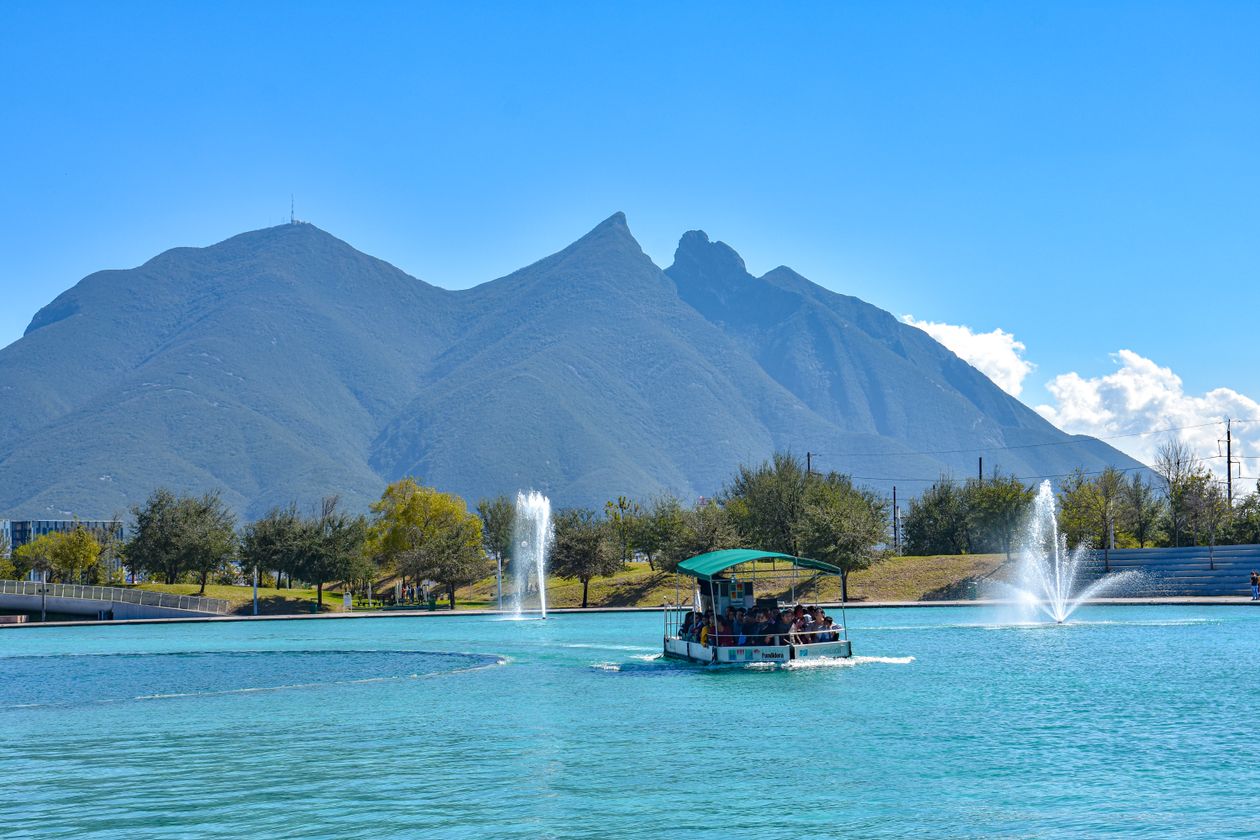 Barco navegando el Paseo Santa Lucía con las montañas de Monterrey al fondo
