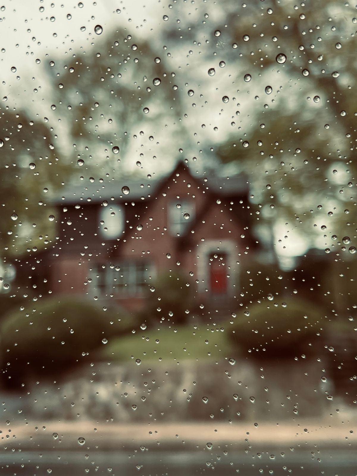 Gotas de lluvia sobre una ventana con una casa al fondo, ambiente húmedo tropical