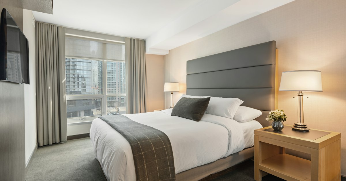 A modern hotel guest room with a neatly made bed and warm lighting