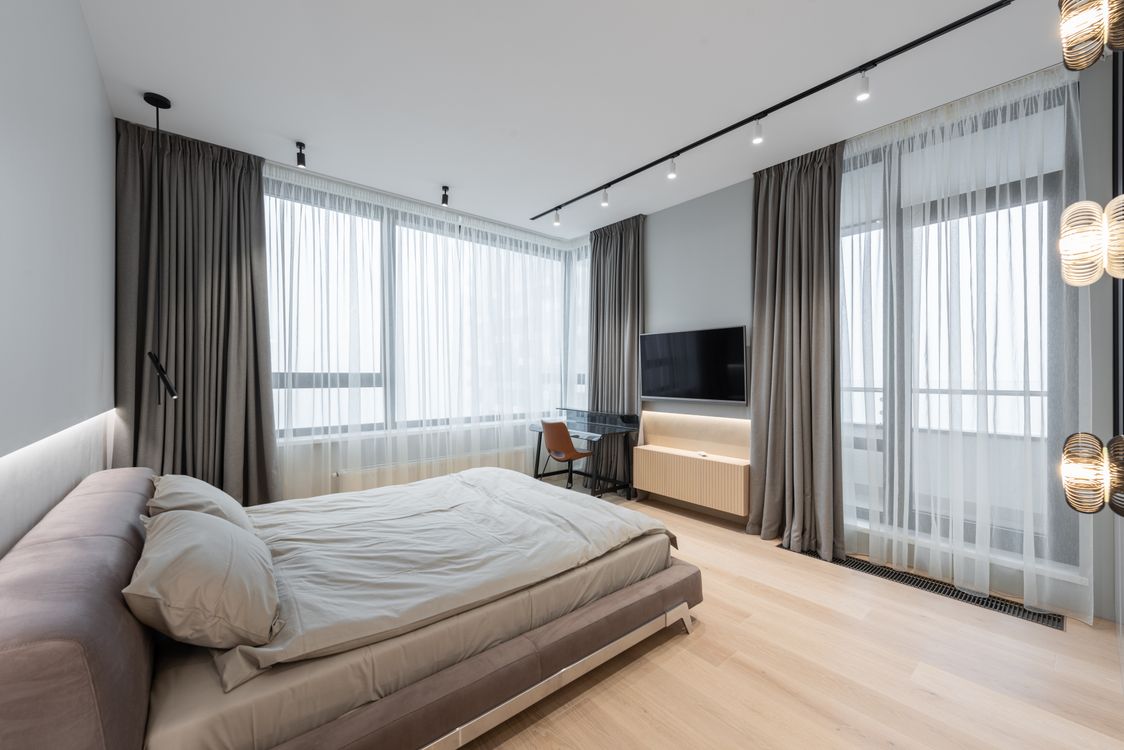 Modern hotel bedroom with floor-to-ceiling curtains and natural daylight through large windows
