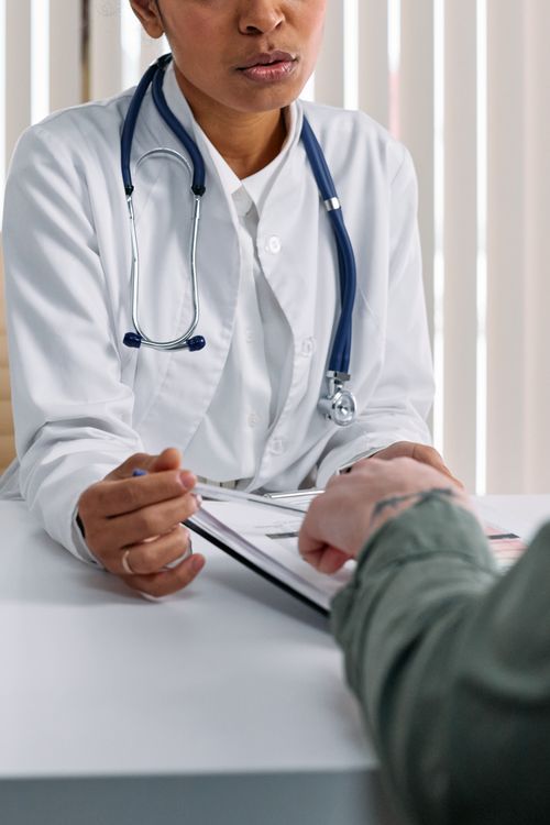 Manos de médico y paciente sobre mesa durante consulta con documentos médicos